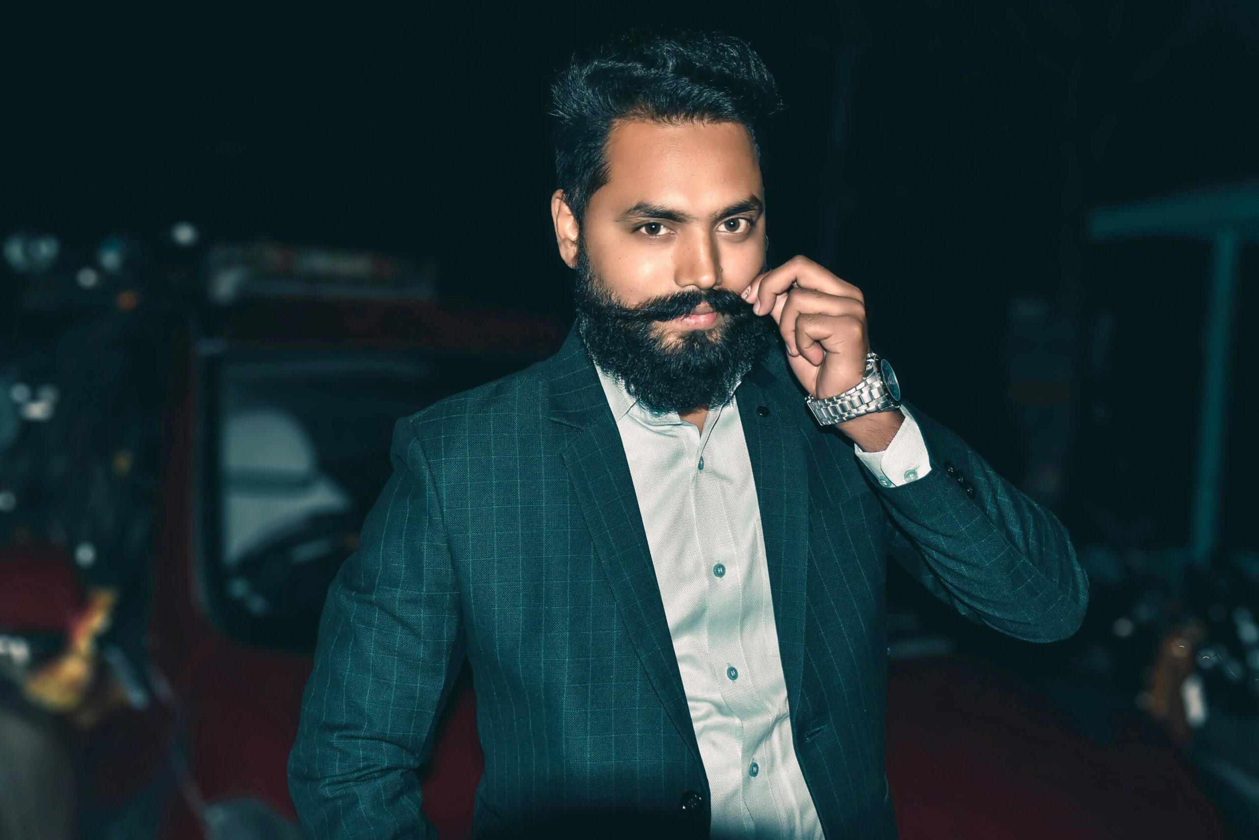 Portrait of a stylish man with a beard in a suit posing at night outdoors.